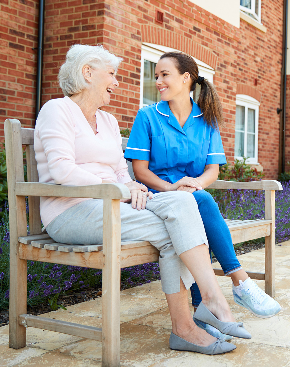 Nurse and resident chatting on an outdoor park bench.