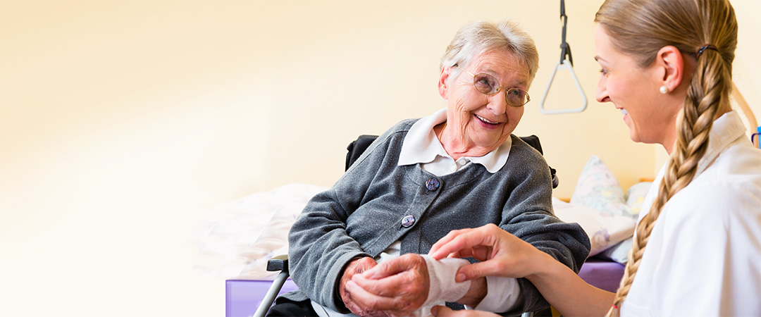 Healthcare worker with long blond braid with wrap around senior woman's wrist.